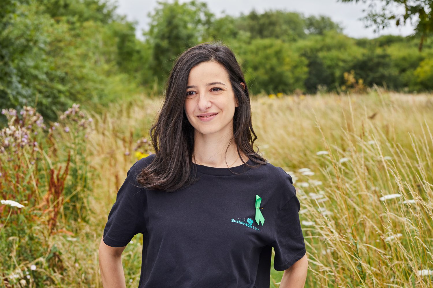 Smiling woman with dark hair outdoors wearing a Sustainable Film t-shirt with a green ribbon