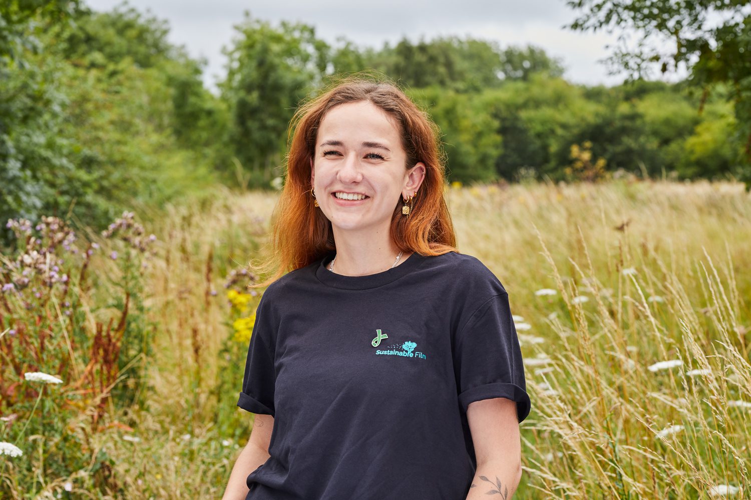 Smiling woman standing in a wildflower meadow wearing a Sustainable Film t-shirt