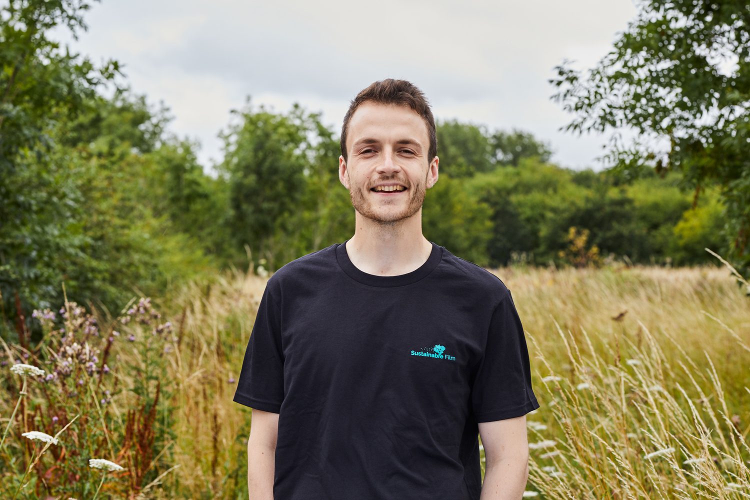 Smiling man standing outdoors in a field wearing a Sustainable Film t-shirt