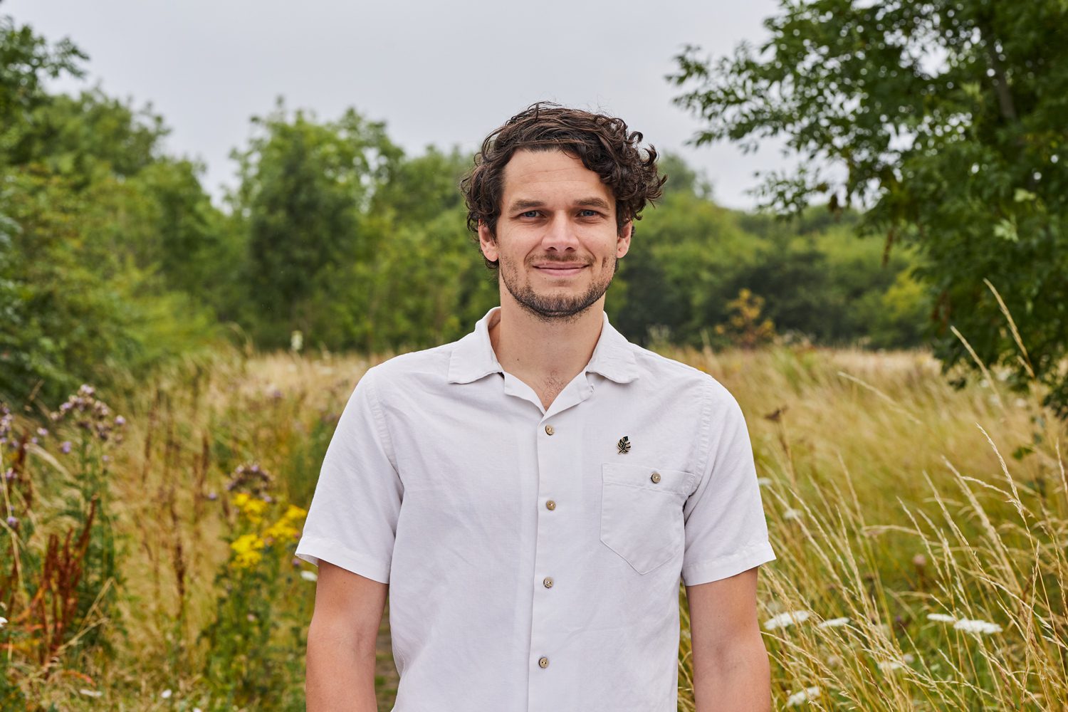 Man in white shirt standing outdoors in natural grassy area